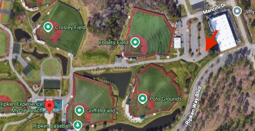 Satellite map of Ripken Experience showing the recommended venue meetup area marked with a red arrow at the parking area beside the large white building off Ripken Way Blvd